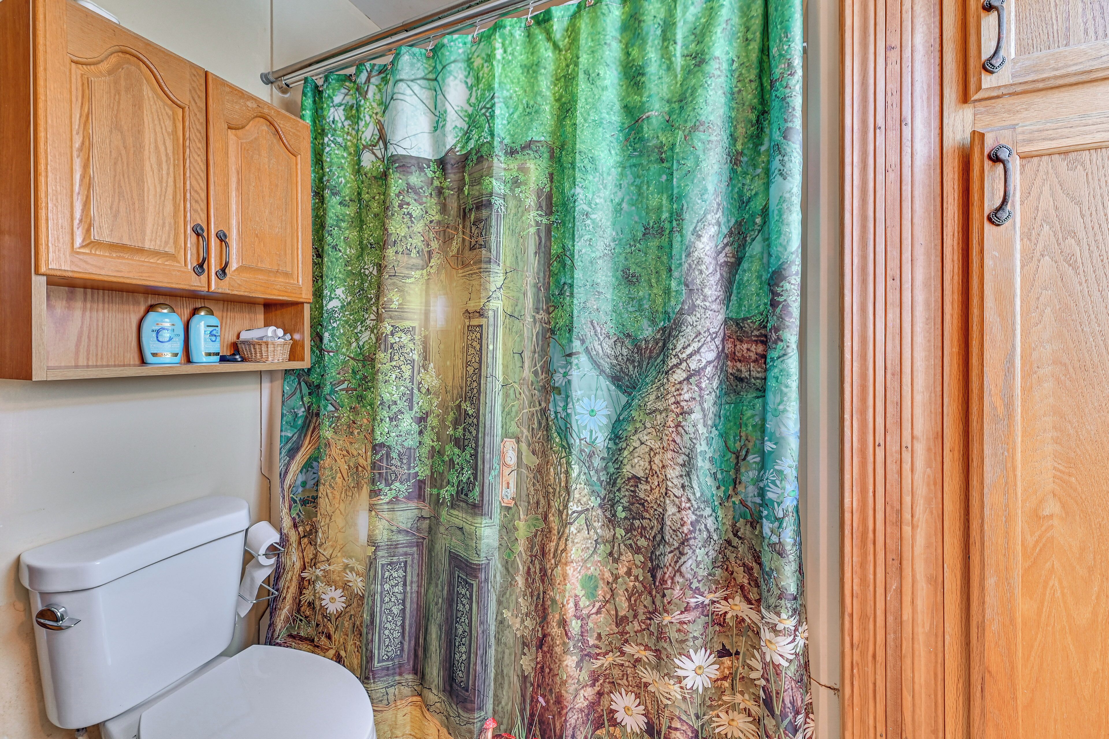 A bathroom with a toilet, wooden cabinets, and a shower curtain with a forest design.