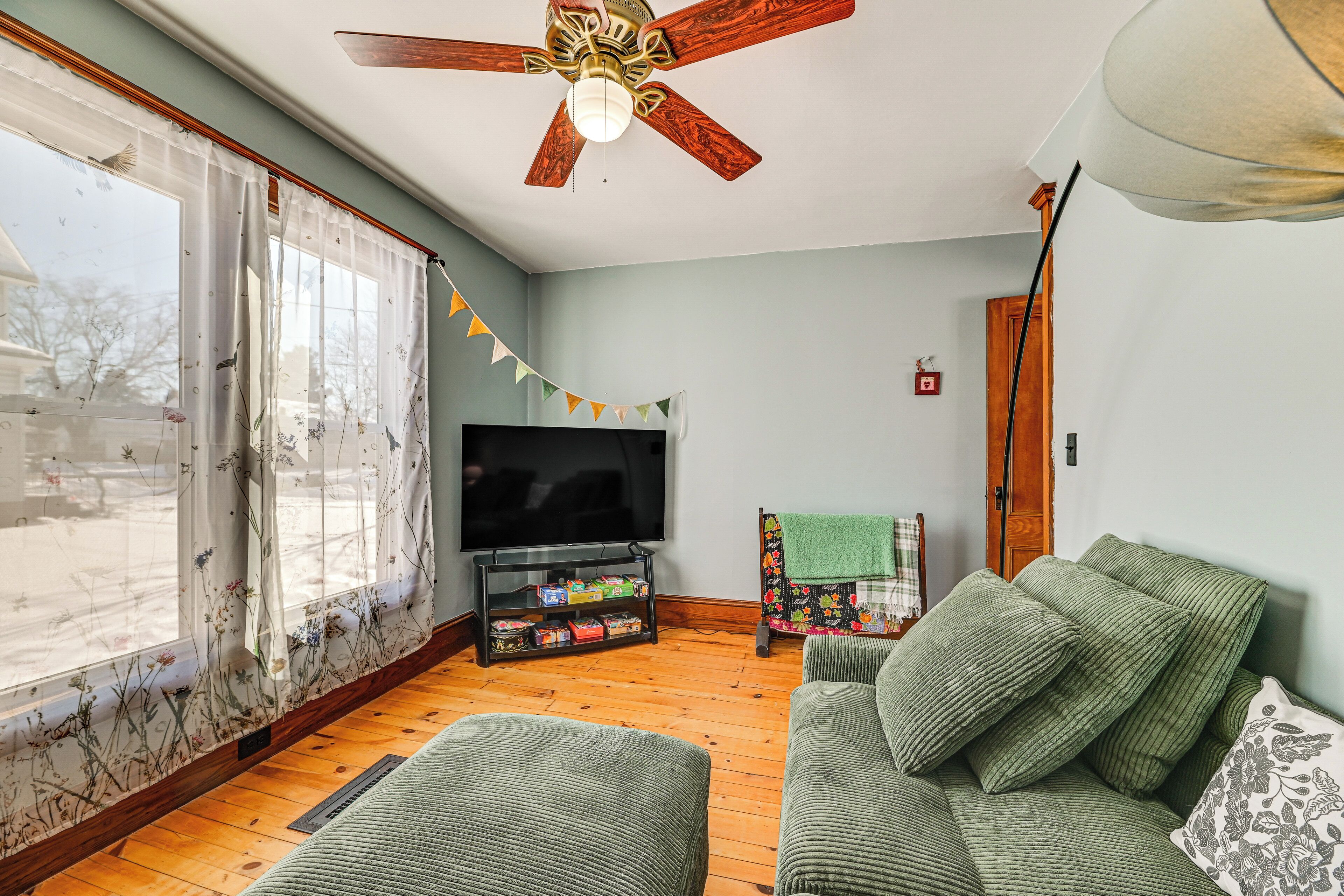 A living room with a wooden floor, a green sofa, a television, and a ceiling fan.