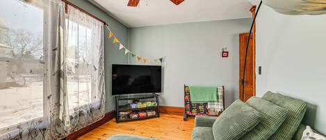 A living room with a wooden floor, a green sofa, a television, and a ceiling fan.
