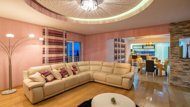 Una sala de estar moderna con un sofá modular, un comedor y una cocina visible a través de una puerta abierta.