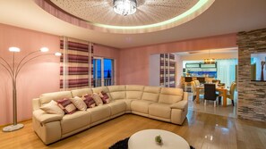 A modern living room with a sectional sofa, a dining area, and a kitchen visible through an open door. - Six Bedroom Villa with Pool,Sauna&Jacuzzi (Kaštel Sućurac)