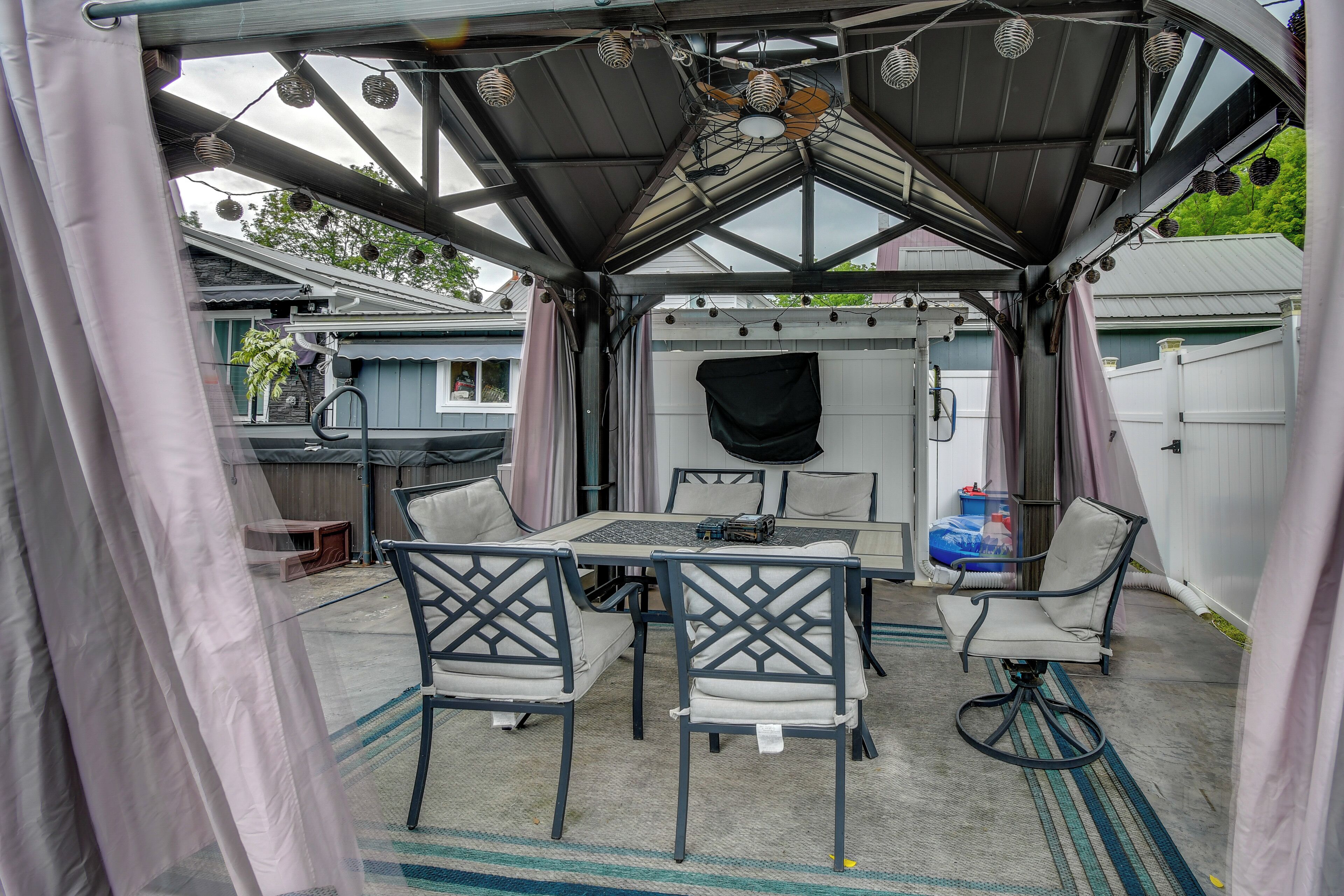 Un espace extérieur abrité, avec une table et des chaises, un ventilateur de plafond et des guirlandes lumineuses.