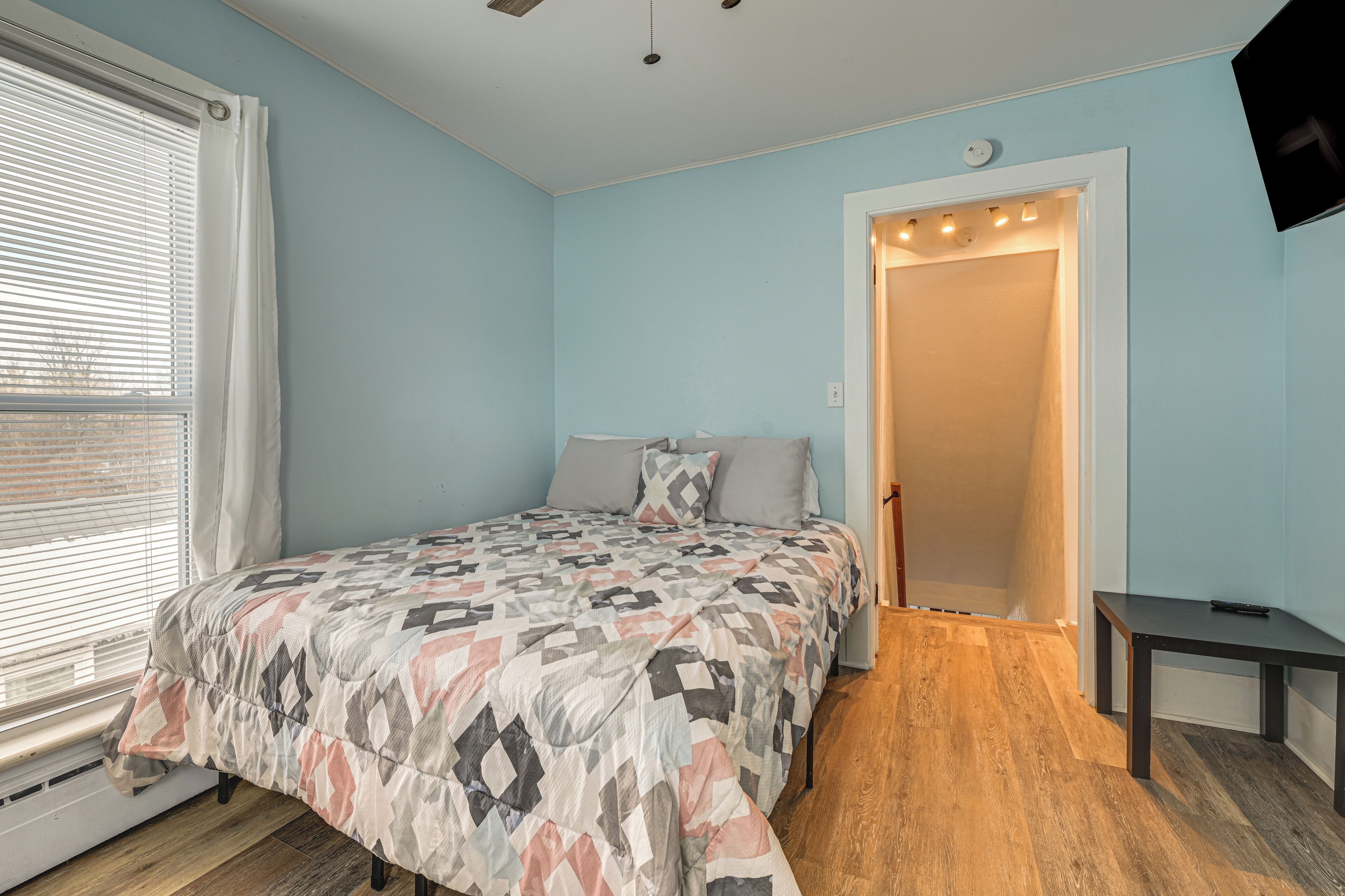 A bedroom with a bed, a nightstand, a TV, and a window with blinds.
