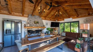 Ein rustikales Interieur mit Kamin aus Stein, Holzbalkendecke, einer modernen Küche und einer gemütlichen Sitzecke mit Sofa und Beistelltisch.