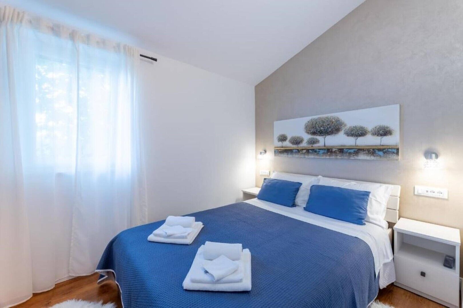 A bedroom with a large bed, white nightstands, and a painting on the wall.