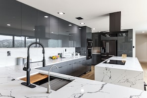 A modern kitchen with dark cabinetry, a marble countertop, and a built-in oven. - Luxurious Austin Hideaway! 4,400-sq-ft Estate (Austin)
