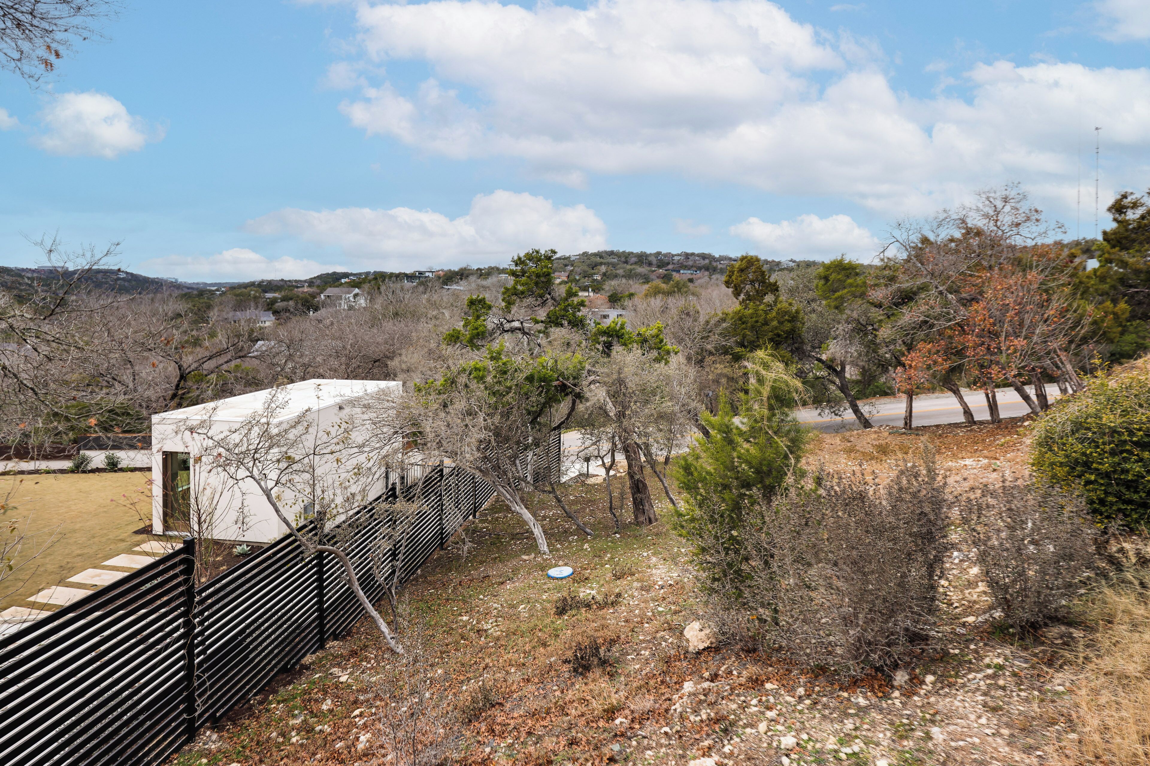 A fenced outdoor area with a white building, trees, and a clear sky.