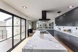 A modern kitchen with a large island, dark cabinets, and a stone wall. - Luxurious Austin Hideaway! 4,400-sq-ft Estate (Austin)