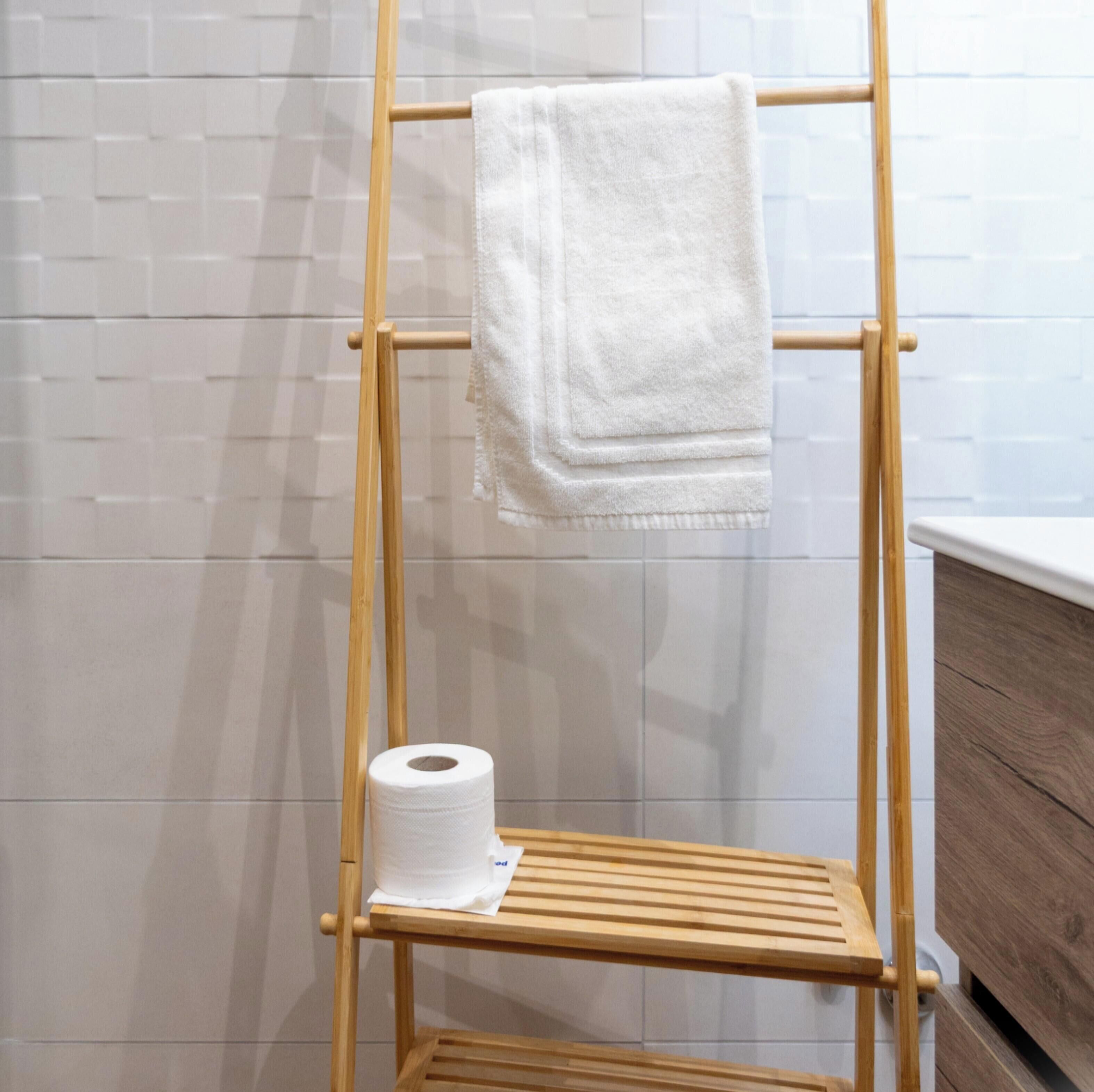 A wooden towel rack with a white towel and a roll of toilet paper.