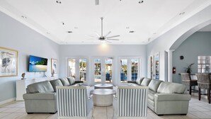 A spacious living room with a large TV, comfortable seating, and a view of the outdoor pool area. - St. Croix at Pelican Marsh (Naples)