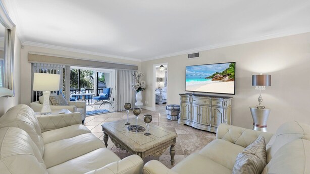 A spacious living room with a large TV, comfortable seating, and a view of the outdoors. - Harborside Terrace at Park Shore (Naples)