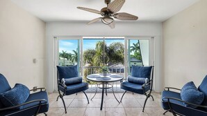 A balcony with two blue chairs, a table, and a ceiling fan. - Harborside Terrace at Park Shore (Naples)