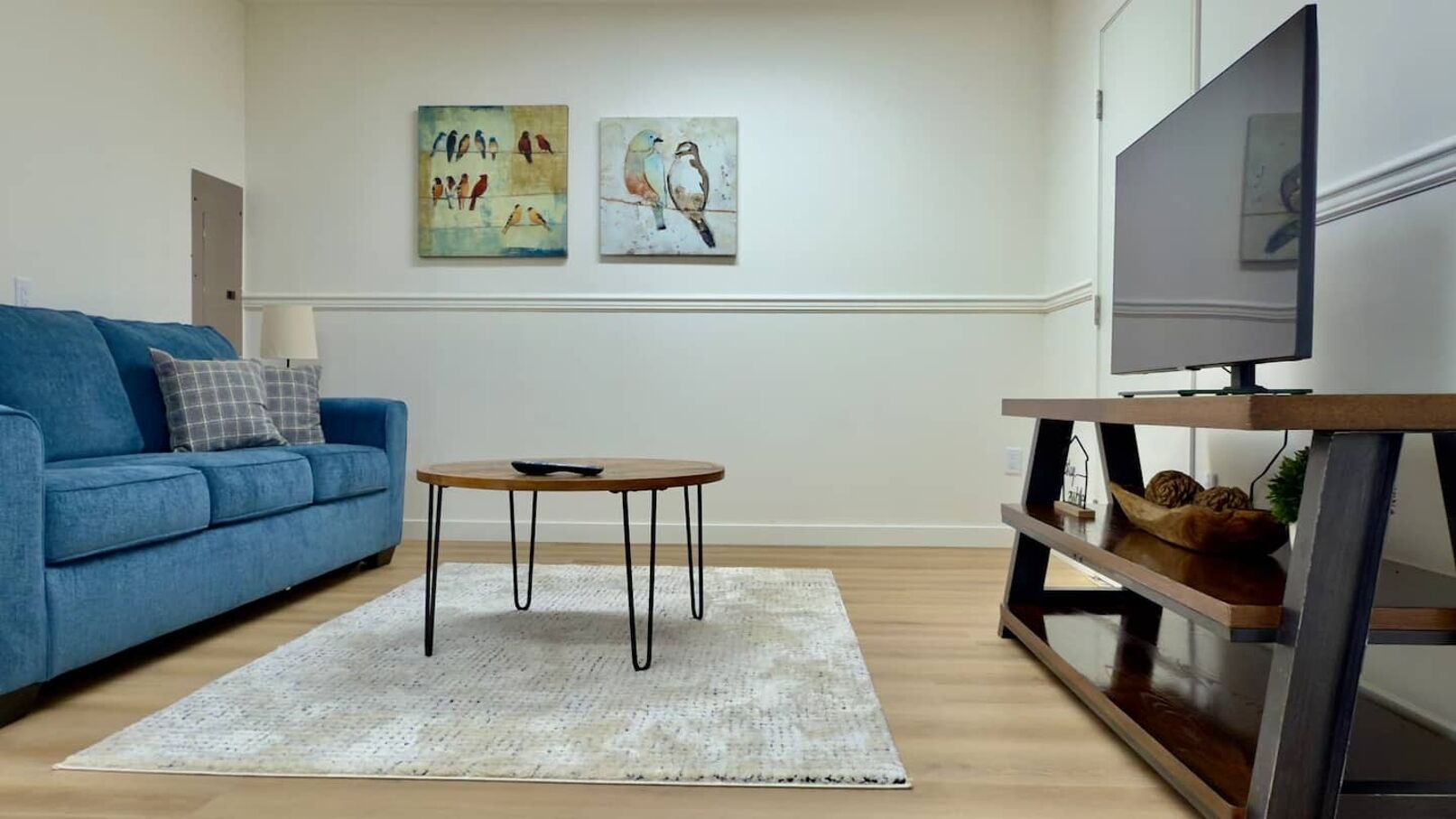 Un salon avec un canapé bleu, une table basse ronde, un tapis blanc et deux tableaux accrochés au mur.
