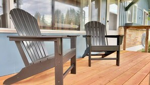 A wooden deck with two Adirondack chairs and a table, overlooking a scenic view. - 3BR Lacey home with bonus room, workspace, fenced yard & patio near trail, shops, and I-5. (Lacey)