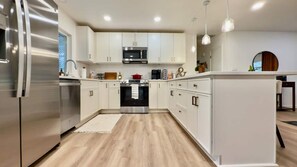 A modern kitchen with white cabinetry, stainless steel appliances, and a wooden floor. - 3BR Lacey home with bonus room, workspace, fenced yard & patio near trail, shops, and I-5. (Lacey)