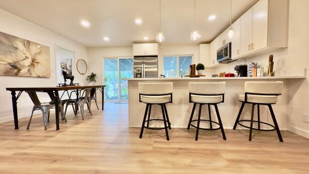 A modern kitchen with a dining area, featuring a bar stool setup, a refrigerator, and a large window. - 3BR Lacey home with bonus room, workspace, fenced yard & patio near trail, shops, and I-5. (Lacey)