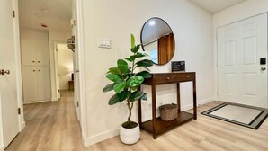 A hallway with a potted plant, a console table with a basket, a round mirror, and a white door. - 3BR Lacey home with bonus room, workspace, fenced yard & patio near trail, shops, and I-5. (Lacey)