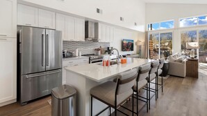 A modern kitchen with stainless steel appliances, a large island with bar stools, and a view of the outdoors through large windows. - New Listing! Peaceful Riverfront Living | Deck with Views | Walk to Downtown (Ridgway)