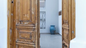 Uma porta de madeira com design tradicional, dando acesso a um corredor com chão ladrilhado e um vaso azul.