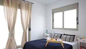 Quarto com cama, bandeja de café da manhã, mesa de cabeceira, luminária e janela com cortinas.