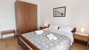 A bedroom with a wooden wardrobe, a bed with a grey floral bedspread, two bedside tables with lamps, and a framed picture on the wall. - Apartment With Pool Near Umag (Umag)