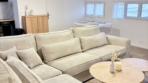 Un salon moderne avec un grand canapé d’angle, une table basse ronde et un coin repas comprenant une table et des chaises blanches.