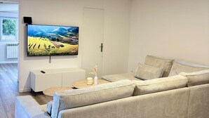 Un salon moderne doté d’un grand téléviseur à écran plat fixé au mur, d’un canapé beige, d’une petite table d’appoint avec un vase et d’un meuble blanc.