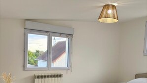 Une chambre à coucher avec un lit, un radiateur, une fenêtre et un luminaire suspendu.