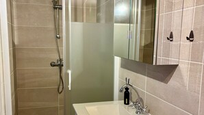 Une salle de bain moderne avec une douche à parois de verre, un lavabo blanc avec un miroir au-dessus, et des murs recouverts de carreaux de couleur beige.