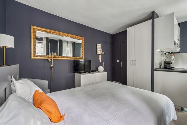 A modern hotel room with a large bed, a TV, a mirror, and a kitchenette. - ID 1051 - Louvre / rue du Pelican (Paris)