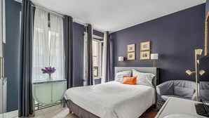 Ein modernes Schlafzimmer mit einem großen Bett, einem Nachttisch, einem Stuhl und einem Fenster mit Vorhängen.