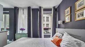 Ein Hotelzimmer mit einem großen Bett, Blick auf die Stadt durch ein Fenster und gerahmte Bilder an der Wand.