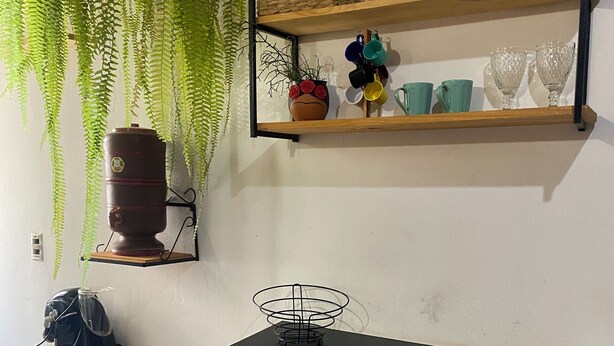A kitchen with a black countertop, two wooden chairs, a coffee machine, a hanging plant, and shelves with dishes and a basket. - Carnival… 5 minutes from the subway, Lapa, beaches, Aterro, Sambadrome. (Rio de Janeiro)