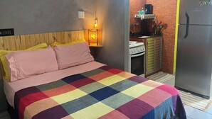 A bedroom with a bed, a nightstand, a lamp, a small kitchenette with a refrigerator, and a brick wall. - Carnival… 5 minutes from the subway, Lapa, beaches, Aterro, Sambadrome. (Rio de Janeiro)