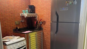 A compact kitchen with a brick wall, a stainless steel refrigerator, a white oven, and a small countertop with various kitchen items. - Carnival… 5 minutes from the subway, Lapa, beaches, Aterro, Sambadrome. (Rio de Janeiro)