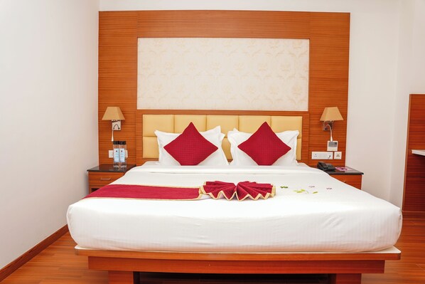 A hotel room with a large bed, wooden headboard, two bedside tables with lamps, and a red and white bedspread. - Hotel Sarovars Legacy  (Bangalore)