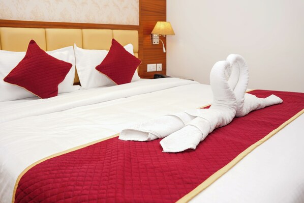 A neatly made bed with a red quilt, white pillows, and a towel arranged in a heart shape. - Hotel Sarovars Legacy  (Bangalore)