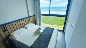 A hotel room with a bed, a window with a view of the ocean, and a wooden headboard. - 02 Quartos no Nomar Carneiros Ecoliving (Tamandaré)