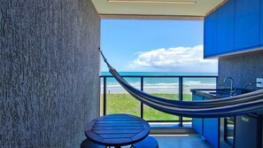 A balcony with a view of the ocean, a hammock, and a small table. - 02 Quartos no Nomar Carneiros Ecoliving (Tamandaré)