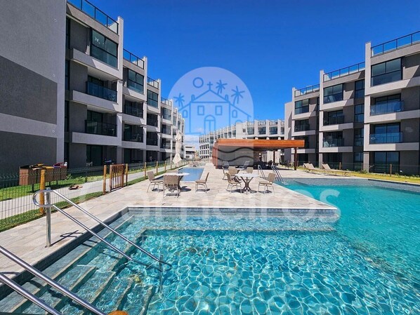 A modern hotel with a swimming pool, outdoor seating, and a clear blue sky. - 02 Quartos no Nomar Carneiros Ecoliving (Tamandaré)