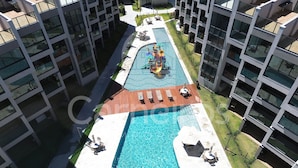 A modern building with a central swimming pool, outdoor seating, and a children's play area. - 02 Quartos no Nomar Carneiros Ecoliving (Tamandaré)