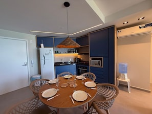 Een moderne keuken met blauwe kastjes, een witte koelkast en een eethoek met een houten tafel gedekt voor zes personen.