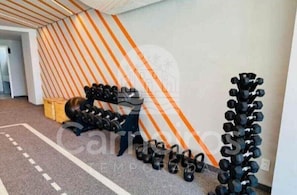 Ein Fitnessraum mit Trainingsgeräten, einer strukturierten Wand und einem Teppichboden.