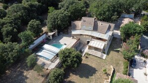 Uma casa de dois andares com piscina, rodeada por árvores densas.