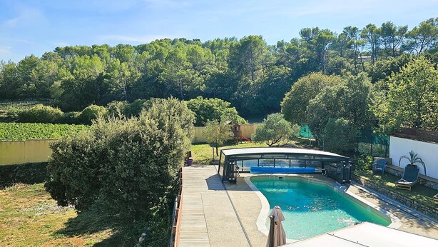 Piscina com deck de madeira e área coberta, rodeada por vegetação exuberante e árvores.