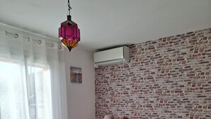 Quarto com cama de madeira, parede com padrão de tijolos, janela com cortinas leves e luminária pendente.