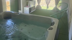 Uma banheira de hidromassagem em um quarto com porta verde, uma pequena prateleira com objetos decorativos e uma cadeira.