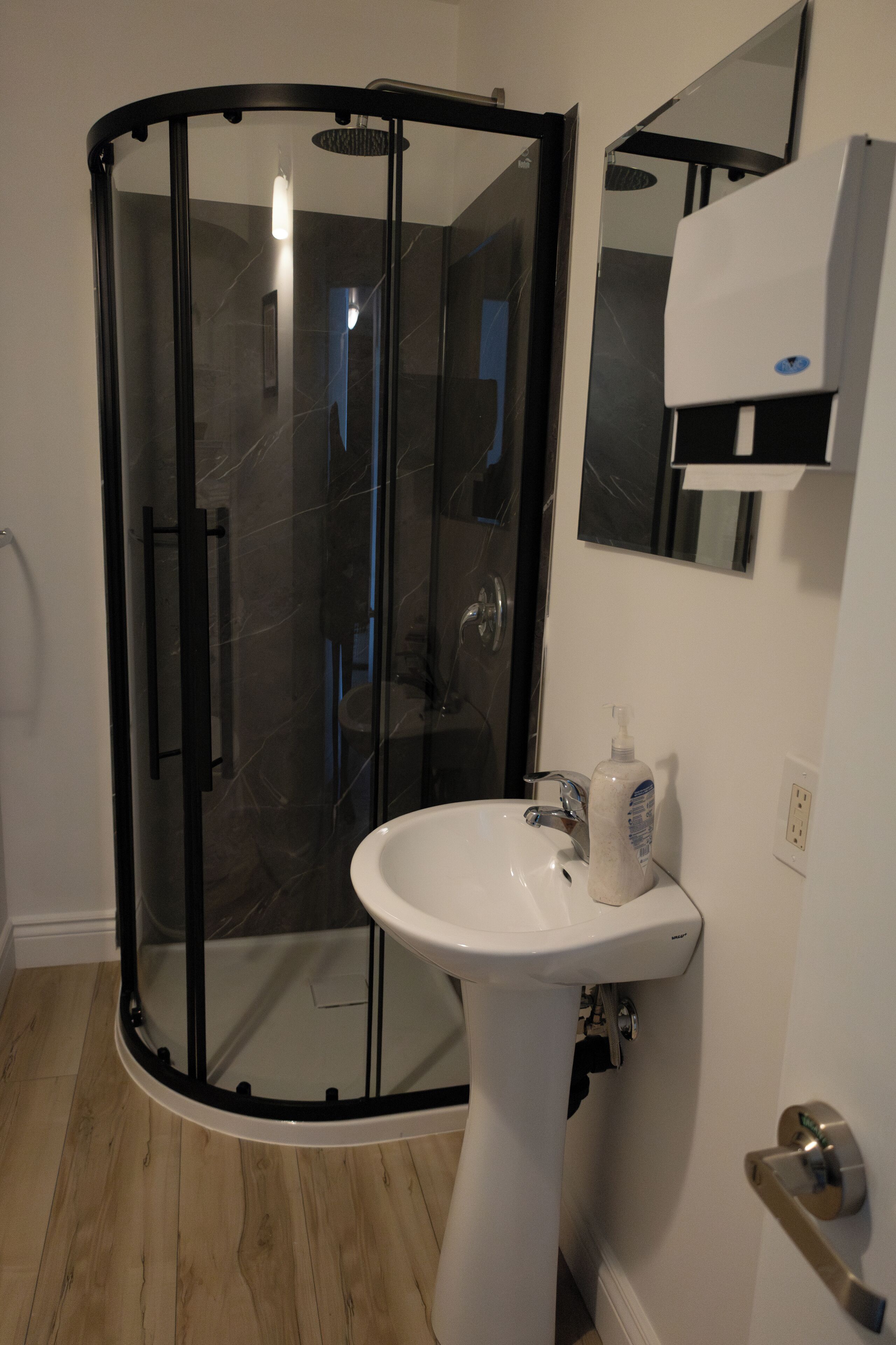 A modern bathroom with a glass-enclosed shower, a pedestal sink, and a mirror above the sink.