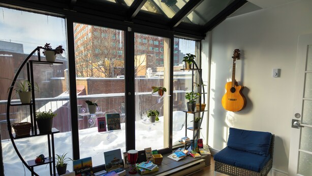 A cozy reading nook with a blue chair, a guitar, and a window seat with books and plants. - Treehouse Hostel (Montreal)