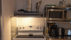 A compact kitchen with a built-in oven and microwave, stainless steel shelves, and a coffee maker. - Treehouse Hostel (Montreal)